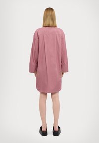 Abito camicia rosa oversize in cotone, con maniche lunghe, taglio dritto e orlo curvo, abbinato a scarpe con plateau nere.