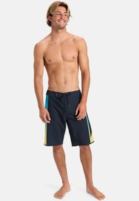 Navy Boardshorts mit flachem Bund, Kordelzug und kräftigen diagonalen Streifen in Türkis und Gelb an den Seiten. Glatte Textur, lässige Passform.