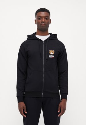 Sweat à capuche noir avec fermeture éclair et logo d'ours, ainsi que le texte "Moschino". Fabriqué en tissu doux avec des poignets côtelés et des poches avant.