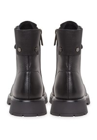 Bottines en cuir noir avec semelles épaisses et tirettes de fermeture éclair, vues de dos montrant des brides de cheville boutonnées.
