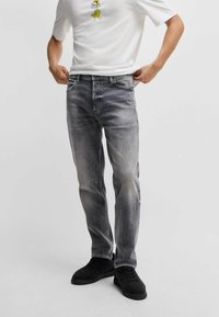 Lidt slidte grå denimjeans med regular fit, fem lommer og mellemhøj talje, parret med en hvid t-shirt med et tegnefilmsdesign.