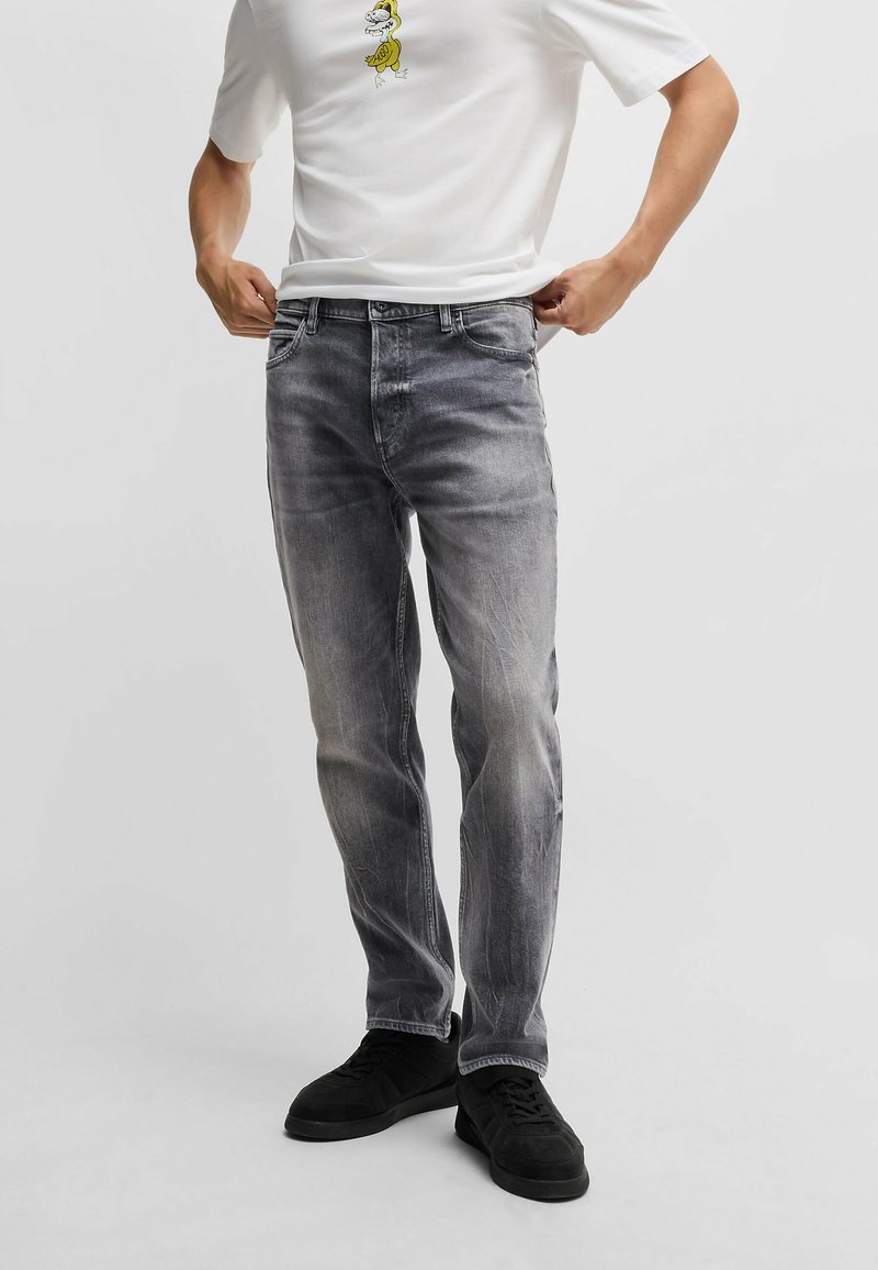 Lidt slidte grå denimjeans med regular fit, fem lommer og mellemhøj talje, parret med en hvid t-shirt med et tegnefilmsdesign.