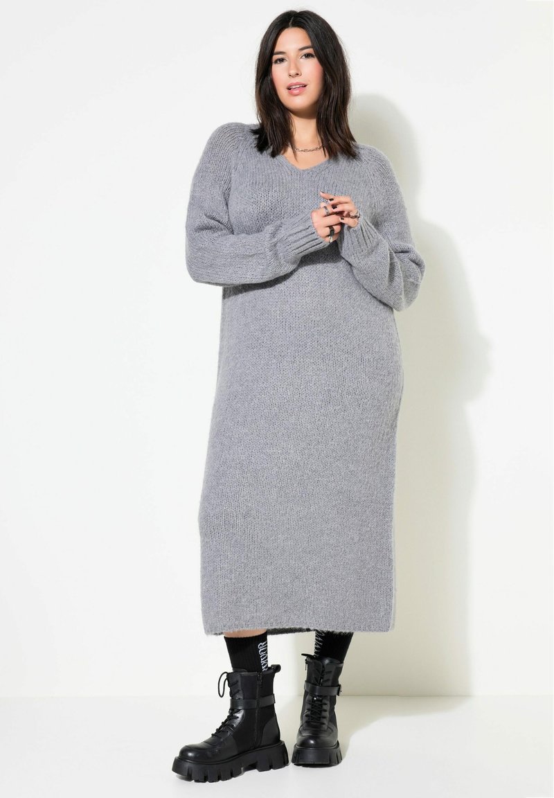 Robe en tricot grise avec une longueur mi-longue, un décolleté en V et des manches longues. Associée à des bottes de combat noires à lacets et des chaussettes à motifs.