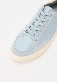 Light blue sneaker made of leather and suede with a smooth toe cap, matching laces, and a textured outsole. Subtle perforations on the side.