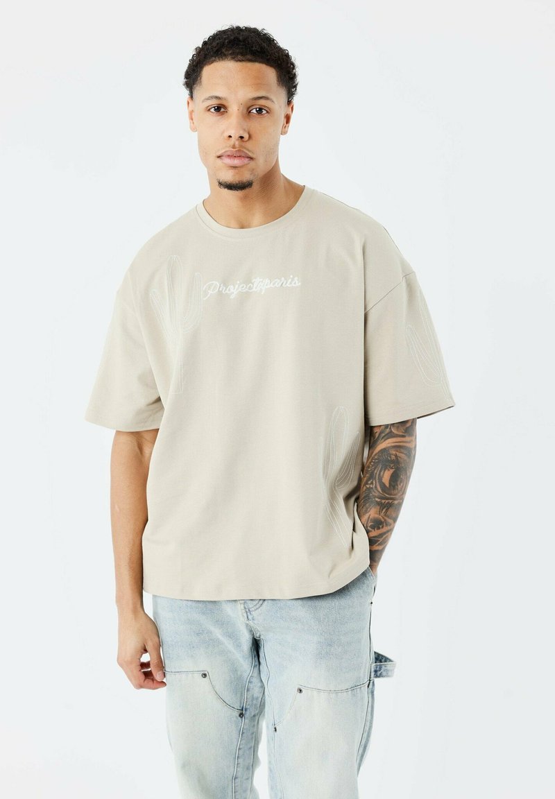 Camiseta de manga corta beige con el logo "Projectparis", diseños de contornos de cactus, cuello redondo y corte relajado. Material de algodón estándar.