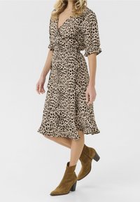 Leopardmönstrad omslagsklänning i tan och svart tyg, med korta volangärmar och en utsvängd nederkant. Kombinerad med bruna mocka ankelskoot.