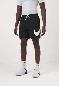 Mustat uimapuvat, joissa on valkoinen Nike-logo vasemmassa jalassa. Ne on valmistettu kevyestä materiaalista ja niissä on joustava vyötärö ja nauha.