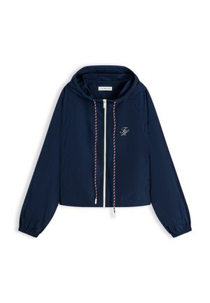 Chaqueta ligera azul marino con capucha, cremallera frontal, cordones rojos y blancos, puños elásticos y un pequeño logo blanco bordado en el pecho.