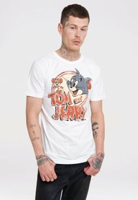 Weißes Baumwoll-T-Shirt mit einem abgegriffenen Graphic von Tom und Jerry, mit auffälliger roter Schrift und runder Gestaltung. Kombiniert mit dunkelblauen Jeans.