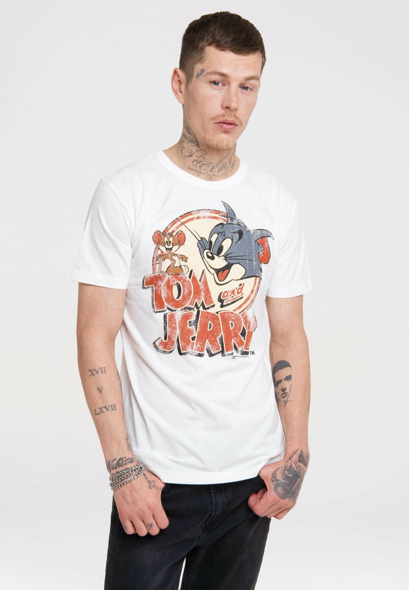 White cotton t-shirt featuring a distressed graphic of Tom and Jerry, with bold red lettering and a round design. Worn with dark jeans.
