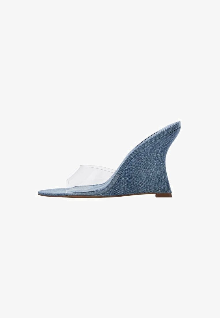 Sandalo con zeppa in denim, dotato di una fibbia in vinile trasparente. Presenta un tacco a zeppa alto e curvo e una tomaia in denim blu texturizzato.