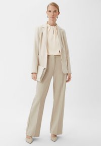 Beige tailored blazer, matching trousers, and cream blouse. Smooth fabric with a gathered neckline detail; paired with a soft clutch and heels.