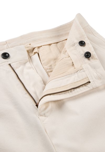 Pantalones beige con cremallera abierta, dos cierres de botón negros en la cintura y forro interior visible.