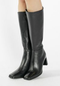 Bocanci negri până la genunchi, din piele netedă, cu vârf pătrat și toc bloc. Caracterizează un design minimalist și o siluetă elegantă.