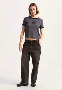 T-shirt grigio corta con rifiniture nere e design grafico; pantaloni cargo scuri e larghi. Entrambi gli indumenti presentano una vestibilità casual e trame di tessuto naturali.