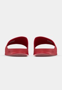 Punaiset liukuunsa soveltuvat sandaalit avoimella mallilla, sileällä kumimateriaalilla ja kuvioidulla pohjalla. Niissä on leveä varvasaukko ja minimalistinen brändäys.