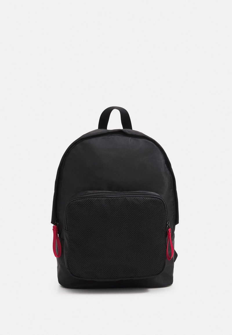 Sac à dos noir de forme arrondie, doté d'une poche avant en maille et de tirettes de fermeture éclair rouges. Fabriqué en matériau léger.