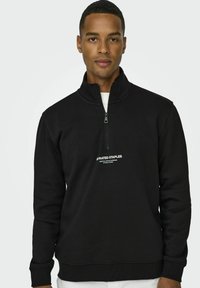 Black zip-up sweatshirt made of soft fabric, featuring a high collar and a small white logo on the chest. Smooth texture, relaxed fit.