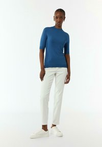 Niebieski sweter z krótkim rękawem o dopasowanym kroju, zestawiony z białymi spodniami slim-fit i białymi sneakersami. Gładka faktura, minimalne detale przeszycia.
