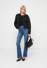 Μαύρο cropped μπουφάν, εφαρμοστό μαύρο τοπ, ανοιχτό μπλε καμπάνα τζιν με λουλουδάτο μοτίβο, μαύρη τσάντα χειρός και μαύρες μυτερές γόβες.