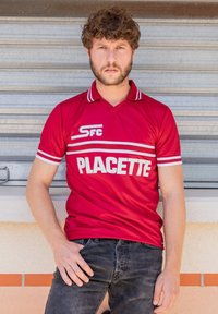 Rode poloshirt met witte strepen op de kraag en mouwen. Bevat witte tekst "PLACETTE" en "SFC." Draag het met donkere jeans.