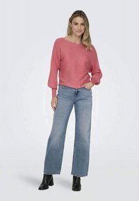 Rosa geripptes Sweater mit weiten Ärmeln, kombiniert mit hellblauen, weit geschnittenen Jeans und schwarzen Stiefeletten. Der Look zeichnet sich durch eine lockere Passform und ein minimalistisches Design aus.