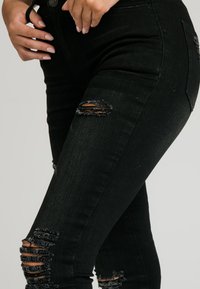 Svarta denimjeans med slitna rivningar vid båda knäna. Hög midja, figurformande, lätt stretch och rena sömnadsdetaljer.