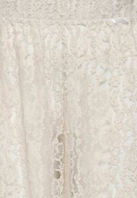 Tissu en dentelle couleur crème avec des motifs floraux complexes et des sections en maille transparente créant un design texturé délicat.