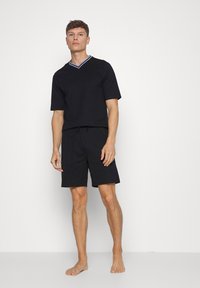 Sort kortærmet V-hals-top med kontrastkant og matchende sorte shorts. Begge dele er lavet af blødt stof, og shortsene har en elastisk talje.