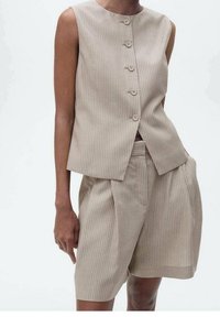 Beżowa kamizelka w paski bez rękawów z pięcioma guzikami i dopasowanymi krótkimi spodniami o wysokim stanie. Gładki materiał z dobrze dopasowanym krojem i czystymi liniami.