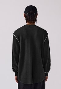 Schwarzes Langarmshirt mit einem strukturierten Waffelmuster, runder Ausschnitt und kontrastierenden weißen Nähten an den Schultern.