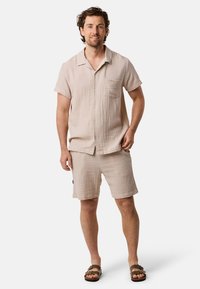 Camicia corta a maniche corte color beige chiaro e pantaloni abbinati, realizzati in tessuto texturizzato. Presenta una tasca sul petto e bottoni sul davanti.