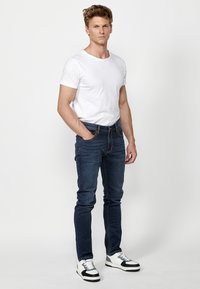 Džíny z denimu v tmavě modré barvě s viditelným švem, úzký střih, spárované s jednoduchým bílým tričkem a černobílými teniskami.