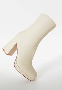 Botín beige crema con tacón cuadrado ancho, material de piel lisa, diseño minimalista, costuras reforzadas y acabado brillante.