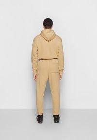 Beige Baumwollkapuzenpullover mit Kordelzug, kombiniert mit passenden Jogginghosen mit elastischem Bund und Gesäßtasche. Schwarze Mütze und Sneakers.