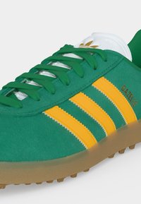 Πράσινο σουέντ αθλητικό παπούτσι Adidas Gazelle με κίτρινες ρίγες, πράσινα κορδόνια, λευκή γλώσσα και καουτσούκ σόλα.
