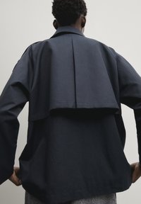 Granatowa, oversize kurtka z szerokim klapem na plecach, długimi rękawami, kieszeniami i usztywnionym kołnierzem, wykonana z lekkiego materiału.