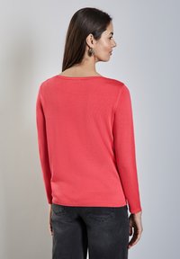 Pull en laine à manches longues, tissu tricoté, décolleté arrondi, poignets et ourlet côtelés, porté avec un pantalon en denim foncé, texture lisse.