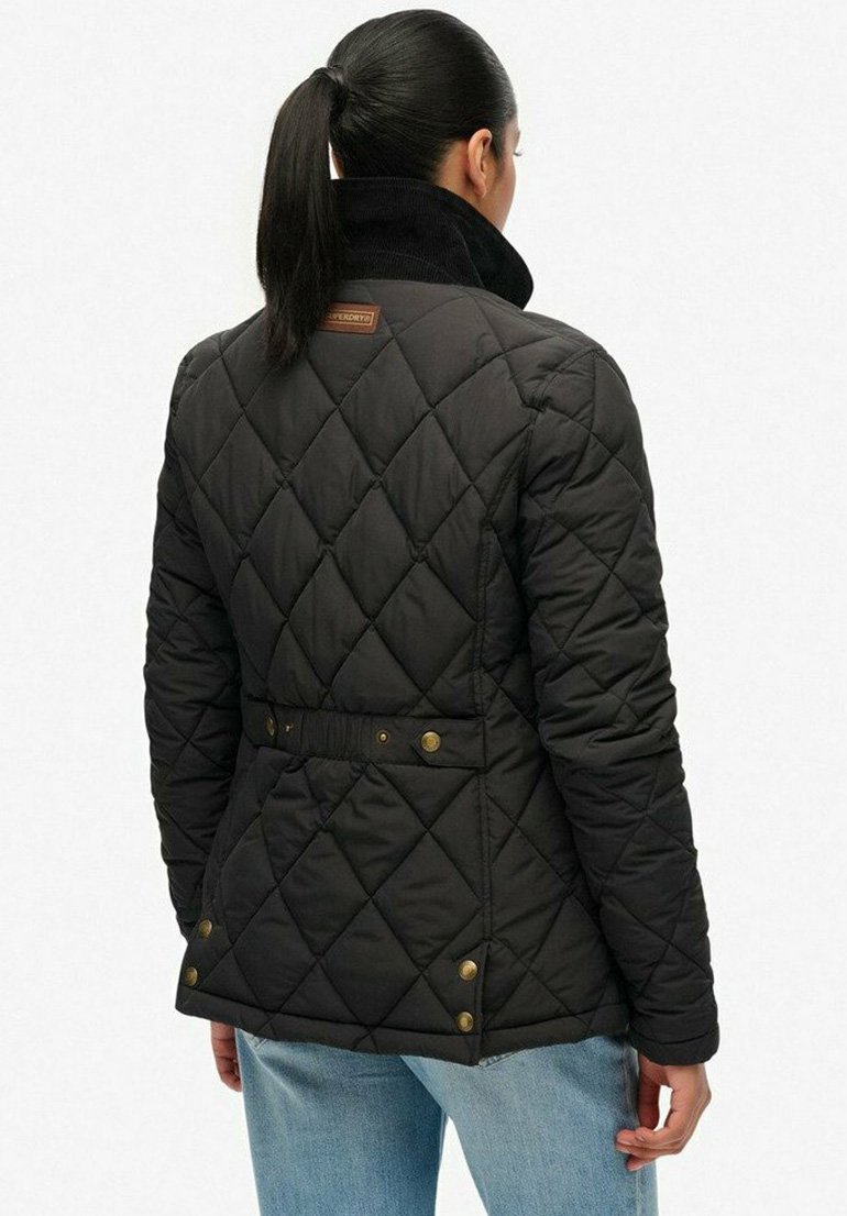Femme avec une queue de cheval noire portant une veste matelassée noire avec des détails de boutons et un jean bleu clair, vue de dos.