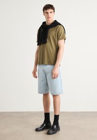 Olivengrønn kortermet t-skjorte, lyseblå denimshorts, svart genser bundet rundt halsen, svarte sokker, svarte loafers, uformell antrekk.