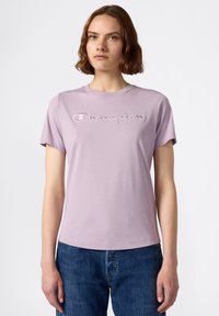 Jasnofioletowy T-shirt z krótkim rękawem, z haftowanym logo "Champion" w ciemniejszym odcieniu fioletu. Gładki materiał bawełniany z okrągłym dekoltem.