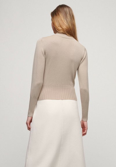 Beige neulepullover, jossa on korkea kaulus, ribattu helma ja istuvat hihat. Sujuva pinta ja selkeä muotoilu, käytetään valkoisen hameen päällä.