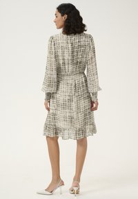 Robe imprimée en crème et gris avec de longues manches à volants, une taille élastique et une jupe fluide se terminant par un ourlet à volants.