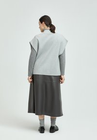 Grauer Wollmix-Oberteil mit übergroßen Schultern, kombiniert mit einem langen, dunklen, kunstledernen Rock. Graue Socken und schwarze Schuhe runden das Outfit ab.