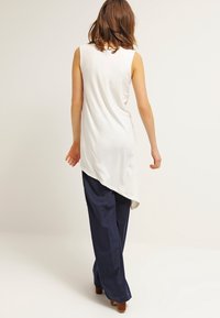 White sleeveless top with an asymmetrical hem paired with loose navy pants, featuring a smooth texture and clean lines.