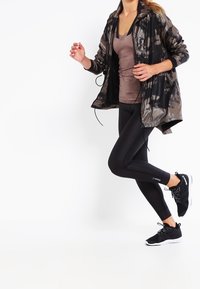 Svart och grå tie-dye träningsjacka, brun figurnära linne, svarta leggings och svarta träningsskor. Jackan har huva och dragkedja.