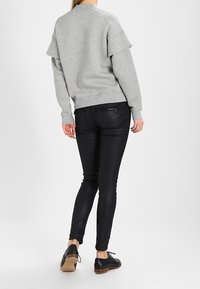 Szara bluza z warstwowanymi krótkimi rękawami, w zestawieniu z dopasowanymi czarnymi spodniami i czarnymi butami. Gładkie tekstury i klasyczny design.