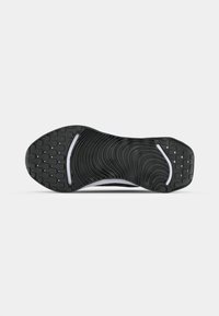 Black athletic shoe sole with a textured rubber surface, featuring a wavy pattern and small grip bumps, accented by white lines.