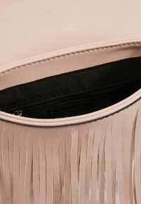 Helles rosa Tasche mit Fransen entlang des unteren Randes. Innenfutter aus schwarzem Stoff, mit Reißverschlusstasche für sichere Aufbewahrung.