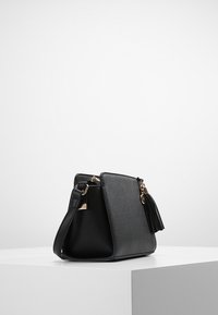 Borsa a spalla in pelle nera con forma strutturata, dotata di hardware oro e un accento con nappina. Texture liscia, di dimensioni medie con tracolla.